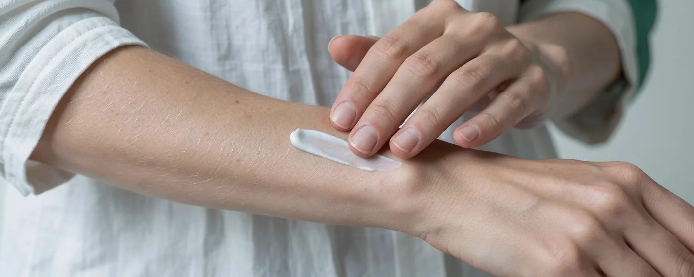 Fingertips gently spread a small dab of plain cream across natural forearm skin.